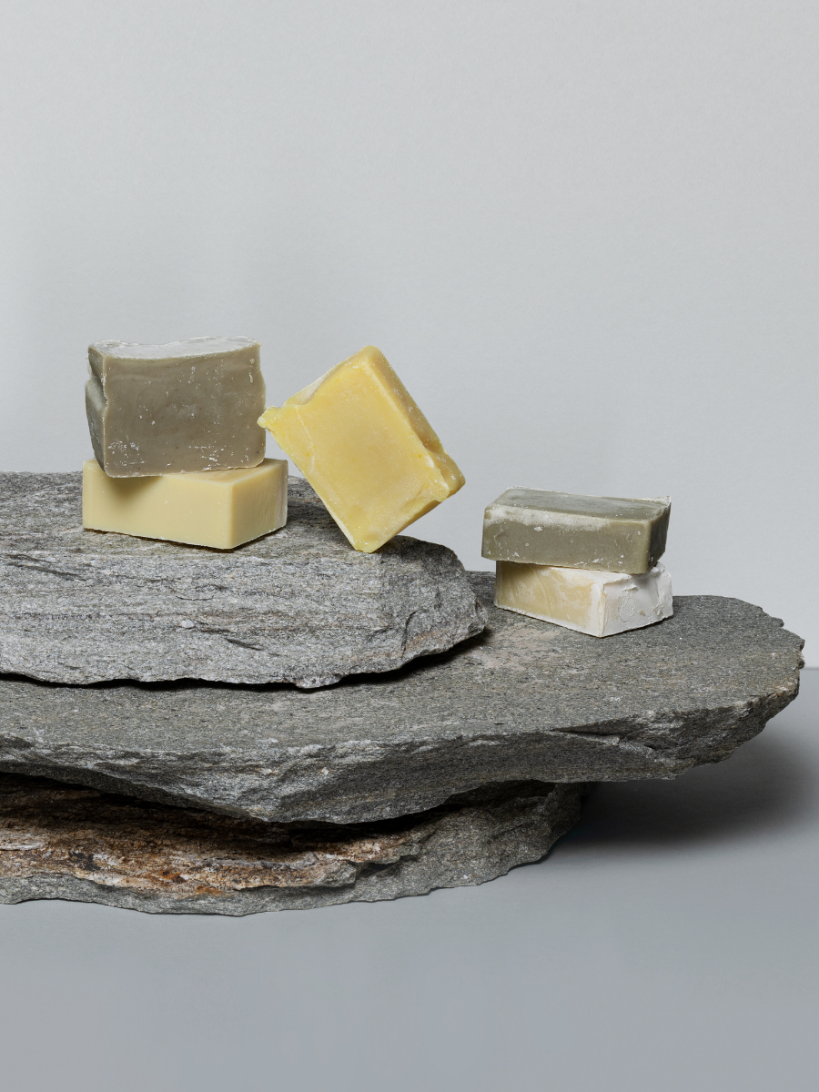 Natural handmade soap bars in various colors stacked on layered gray stones by Magrada Organic Cosmetics