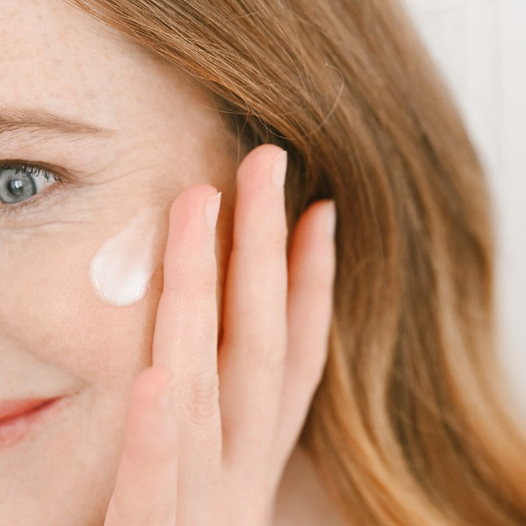 Close-up of woman applying vegan face cream hydrating on her cheek for glowing skin