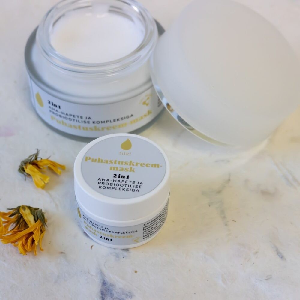 Tilk 2-in-1 cleansing cream mask in white jars with open lid and dried flowers on marble surface